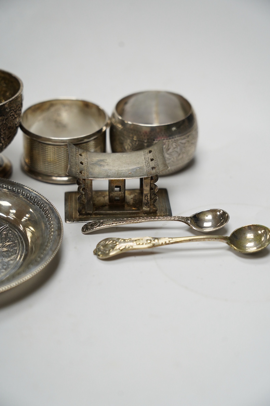 Sundry small silver including five silver napkin rings, and 800 napkin ring, a Victorian silver mustard and salt, an Egyptian small white metal dish, three silver condiment spoons and five plated items. Condition - poor